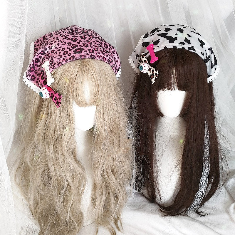 Two long synthetic wigs displayed on mannequin heads, each wearing a different style of animal-print headband. The left wig is light blonde with a pink leopard print headband.